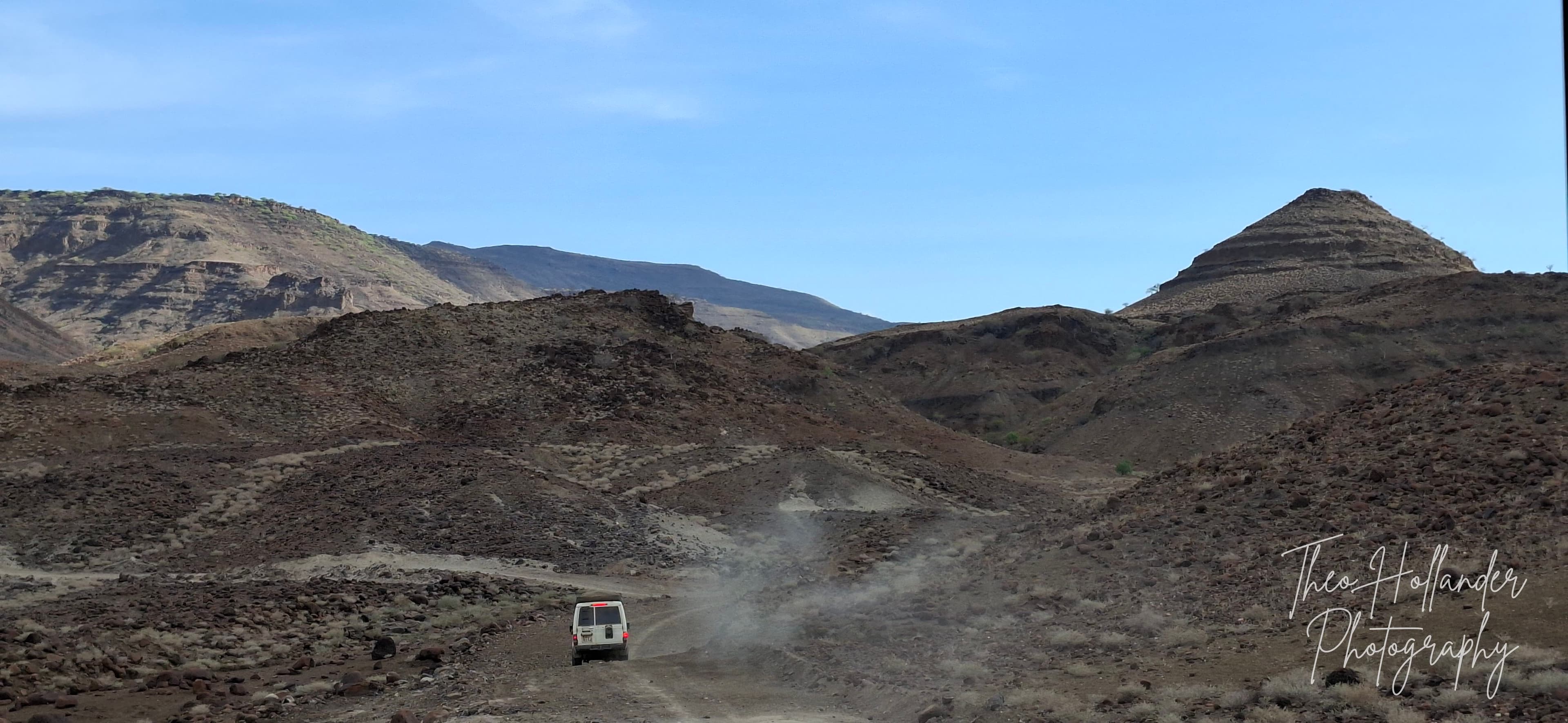 A safari vehicle threading through a volcanic landscape of black rock