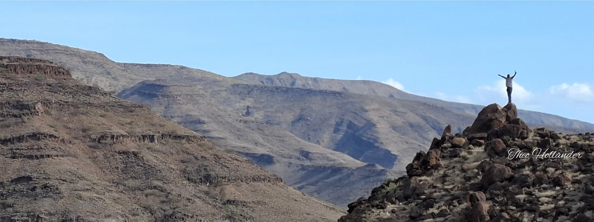 A hiker celebrating atop a rocky ridge in Kenya's remote Suguta Valley
