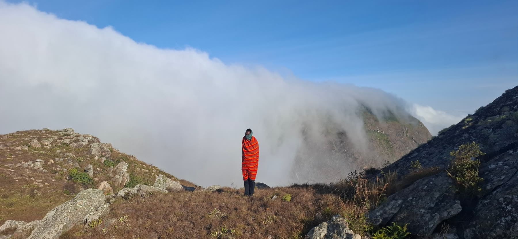 A guide wrapped in an orange Samburu shuka as cloud pours over a Ndoto Mountains ridge