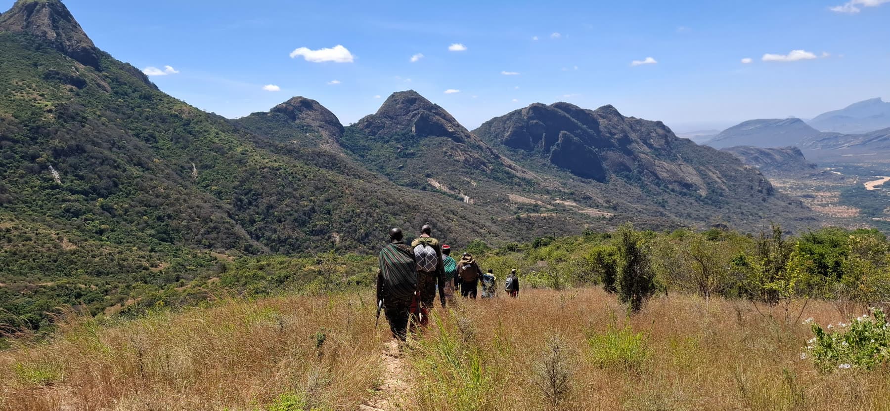 A line of local guides and porters trekking through a valley in the Ndoto Mountains