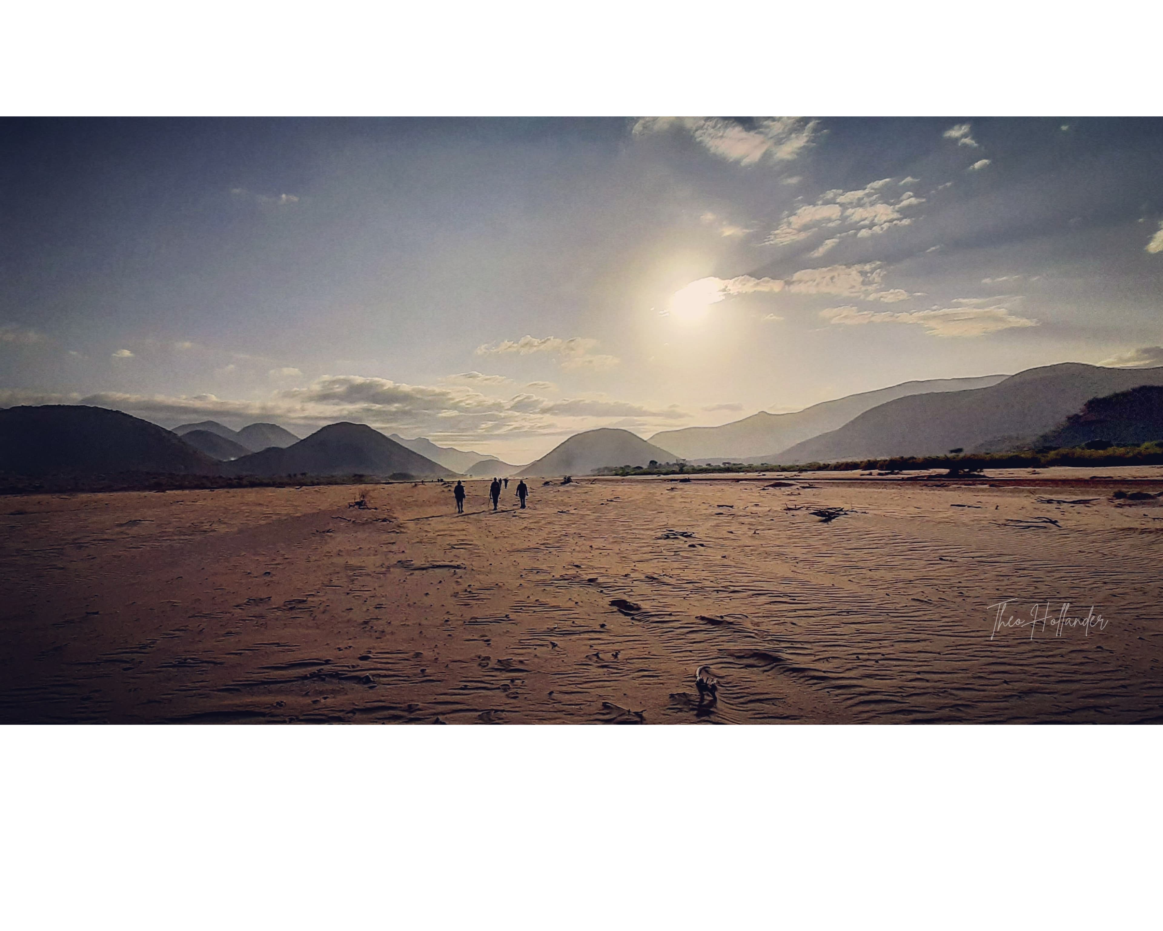 Walking across a wide, sandy desert riverbed near the Ndoto Mountains, mountains silhouetted at sunset (placeholder photo, pending Marsabit route photos)